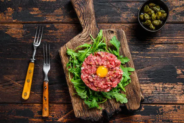 Tartar beef with a quail egg and arugula served on a cutting board. Dark wooden background. Top view.