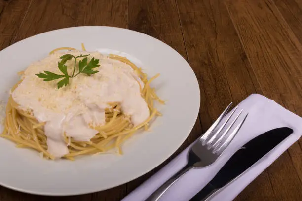 Photo of Pasta with bechamel sauce with grated cheese and parsley leaves. Gourmet close-up photo of popular pasta. Diagonally aligned elements