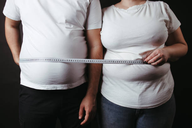 Overweight fat couple wrapped with measure tape Overweight couple standing together wrapped with measure tape. Dieting, family weight loss and health care human abdomen stock pictures, royalty-free photos & images