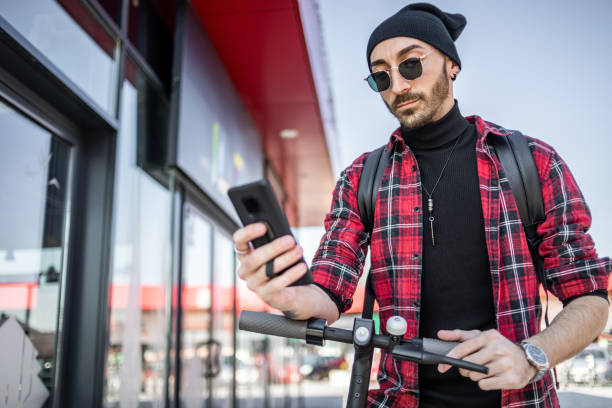 istock A young man on his e-scooter. Technology, ecological concept of mobility. The hipster young man controls the commands on his scooter via an app on his smartphone. 1312190668