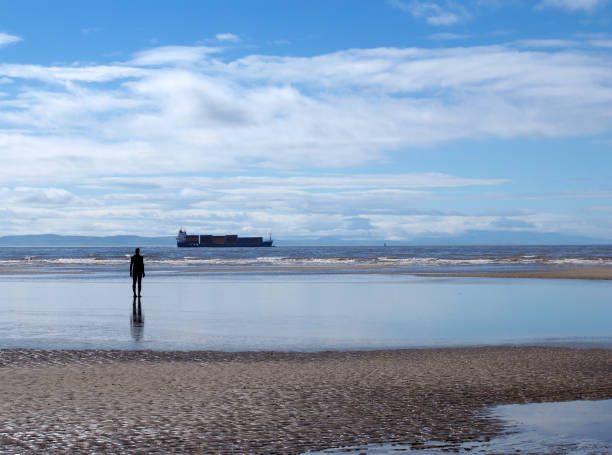 A man standing in the background, silhouetted against the backdrop of shipwrecks in a ship junkyard in Pakistan