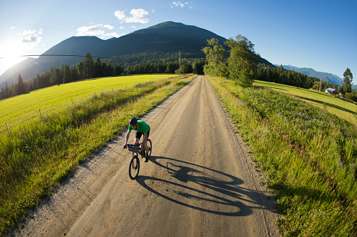A male cyclist goes for a gravel road bicycle ride in British Columbia, Canada. His bicycle has bags strapped to the frame that carry extra clothes, food, and bike tools. His bicycle has a front suspension fork, disc brakes, and wheels and tires suited to riding on rough terrain.