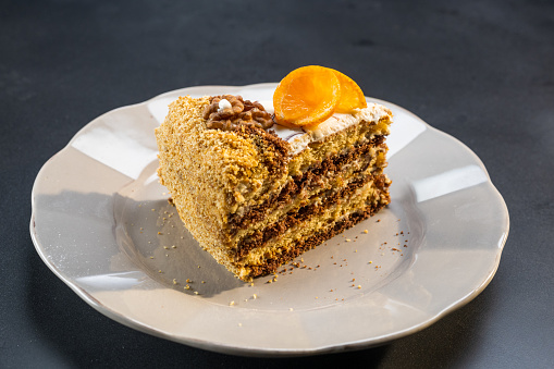 Slice of nuts cake with orange spiral served on white plate. Homemade baked desserts for celebration or birthday concept.
