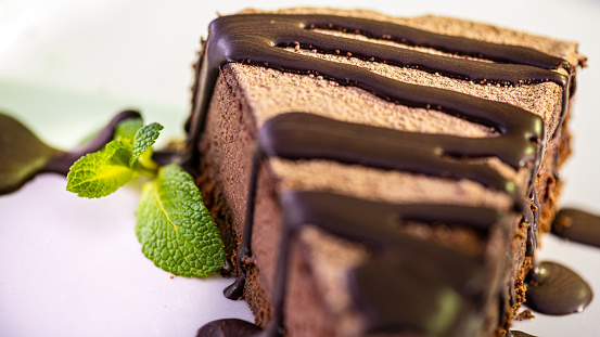 Close-up of chocolate cheesecake with chocolate icing decorated with sprig of lemon balm. Selective focus. Homemade baked desserts for celebration or birthday concept.