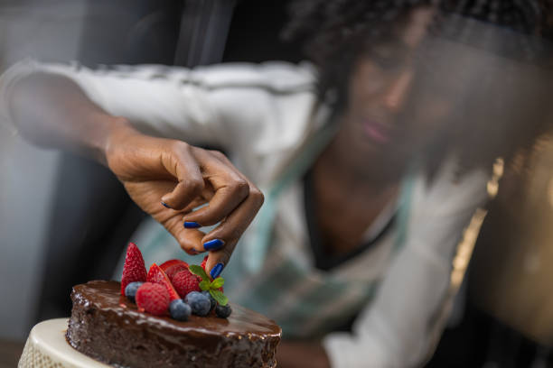 istock Woman adjusting top of multi-tier cake. Adding fresh fruit and green herbs as decoration. 1312202268