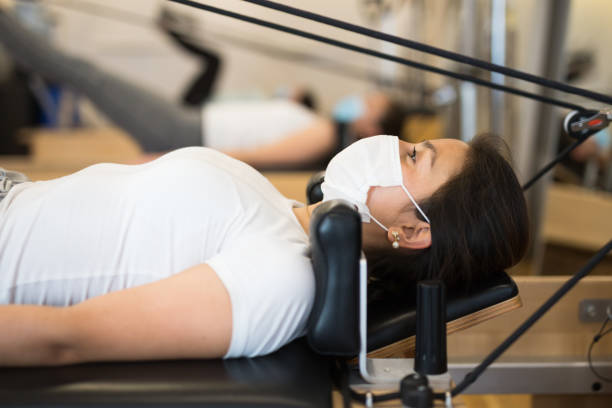 jeune latina dans le masque protecteur pratiquant le pilates sur le réformateur - pilates machine photos et images de collection