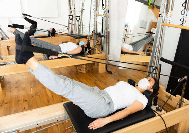 jeune latina dans le masque protecteur pratiquant le pilates sur le réformateur - pilates machine photos et images de collection