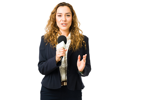 Attractive journalist talking about breaking news with a microphone. Hispanic young woman reporting live for the tv news against a white background