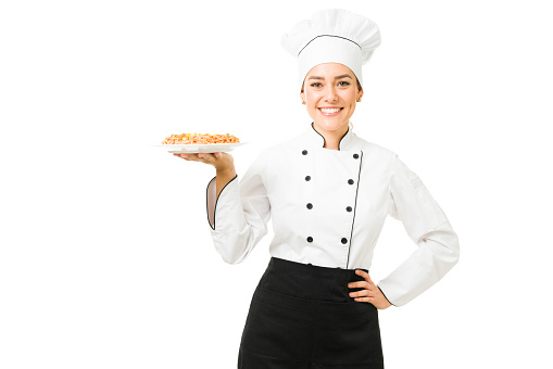 Cheerful chef in a white uniform showing the dinner on a plate. Beautiful young woman working as a cooker of a restaurant and made a tasty spaghetti for lunch