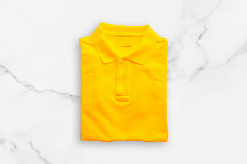Top view of Yellow polo t-shirt on white marble floor background.