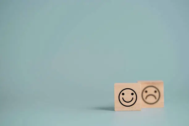 Photo of Smiley face in front of sadness face which print screen on wooden cube block, emotion selection for customer satisfaction and evaluation concept.