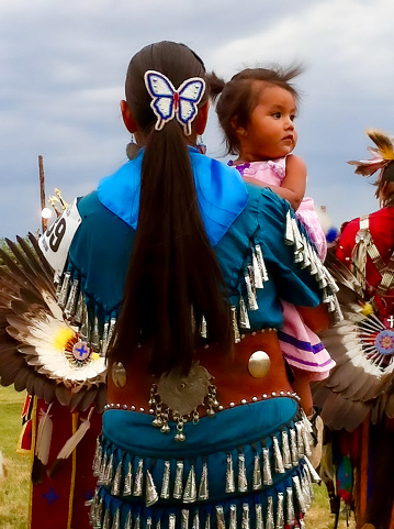 Vertical closeup, seen from behind, of a female dancer, wearing ornate, colorful traditional clothing and her daughter at the annual Taos Pow-Wow in Taos, New Mexico