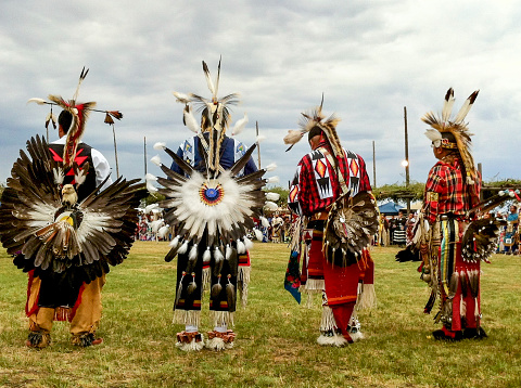 Horizontal closeup of four male native American dancers in a line wearing vibrantly colored, traditional clothing at the annual Taos Pow-Wow in Taos, New Mexico