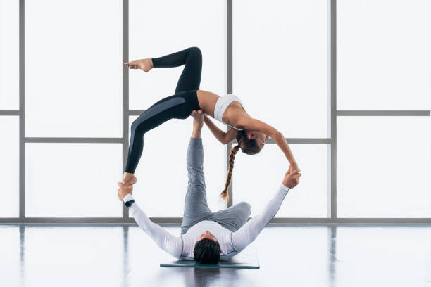 diverse athletic couple caucasian and asian in sportswear practicing acro yoga or yoga partner together in gym and fitness club. Athletic couple healthy and wellness lifestyle. stock photo