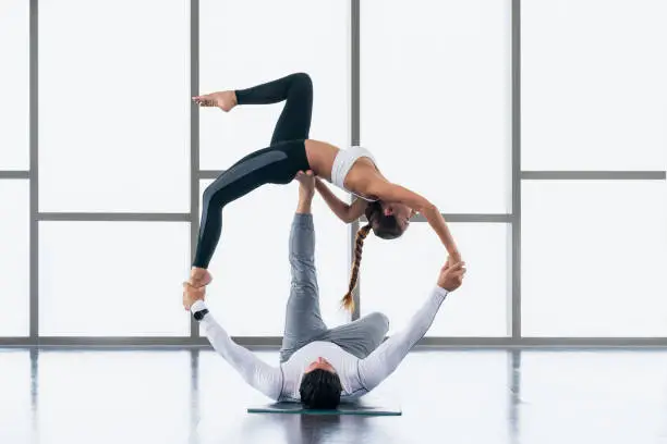 diverse athletic couple caucasian and asian in sportswear practicing acro-yoga or yoga partner together in gym and fitness club. Athletic couple healthy and wellness lifestyle.