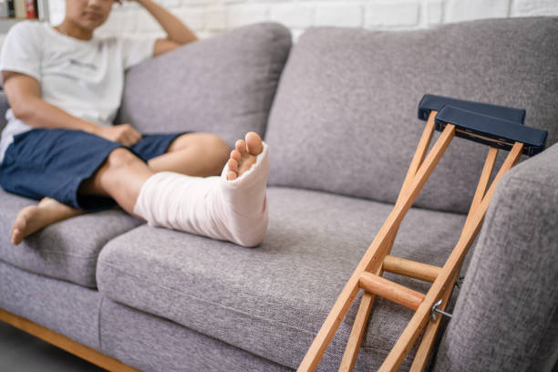 jeune homme asiatique avec une jambe cassée se reposant sur le sofa. fermez-vous vers le haut de la béquille. - blessure physique photos et images de collection