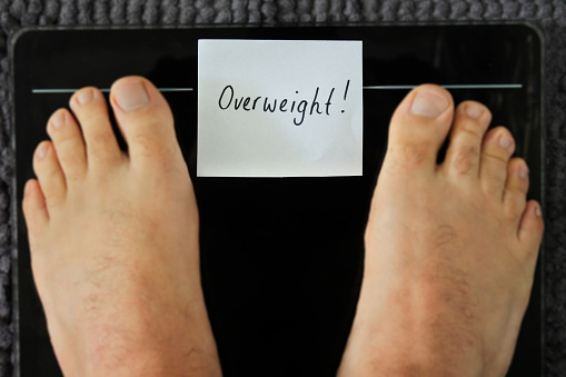 POV (Point of view) of a person standing on a weight scale with sign reading overweight word. Health care concept. Copy space