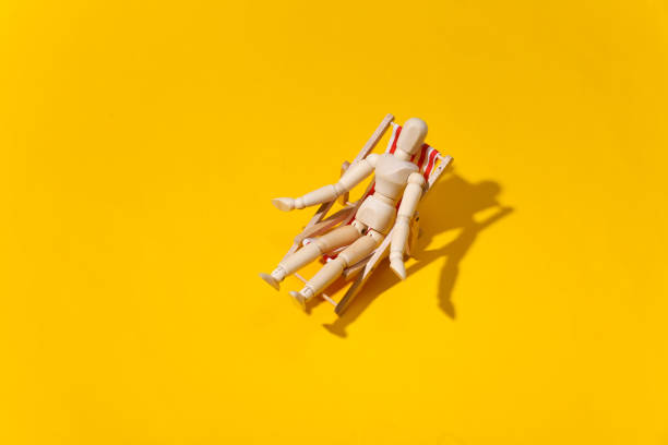 Puppet mannequin sunbathes on the deck beach chair. Yellow studio background. Bright sunny light. Beach Vacation Concept. Summer rest.