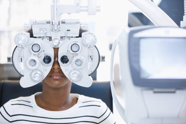 jovem afro-americana exame ocular com oftalmologia diagnóstica em clínica óptica. visão de verificação oftalmica profissional do paciente. máquina de phoropter, verificação de saúde ocular e conceito de oftalmologia. - equipamento óptico - fotografias e filmes do acervo