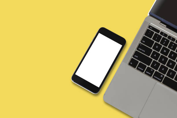 istock Smartphone blank white screen with half laptop on yellow background. Mockup mobile phone empty screen. 1312235873