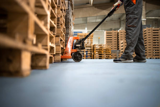 istock Working at warehouse. Low angle view of unrecognizable worker lifting palette with manual forklift. 1312235930