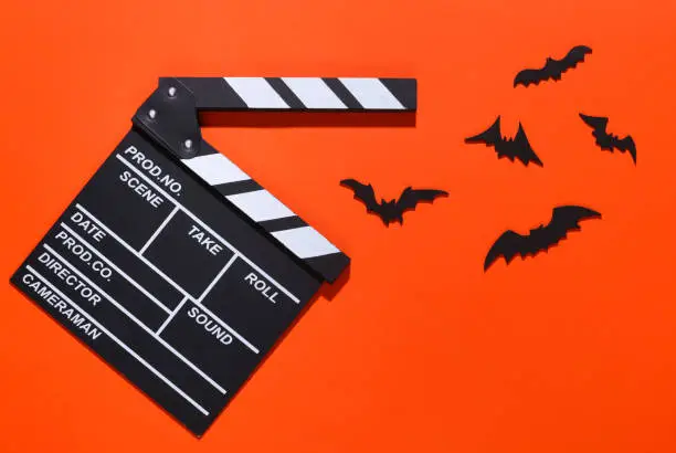 Horror movie, halloween theme. Movie clapperboard and flying decorative bats on brightorange background. Top view, flat lay