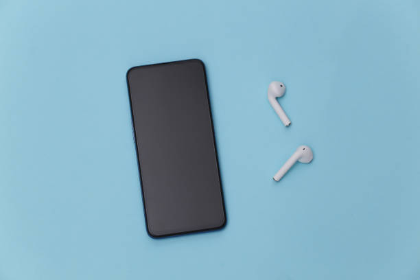 istock Modern smartphone with wireless earphones on blue pastel background. Top view. Flat lay 1312238982