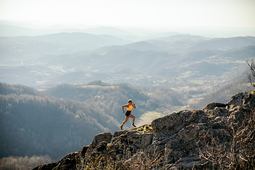 Woman athlete trail runner running and climbing mountain cliff during her training. Extreme terrain.