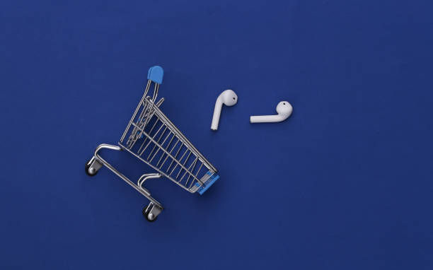 Shopping trolley and modern wireless earphones on classic blue background. Top view. Flat lay stock photo