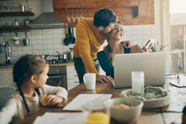 istock Affectionate man kissing his wife while she is working on laptop at home. 1312241519