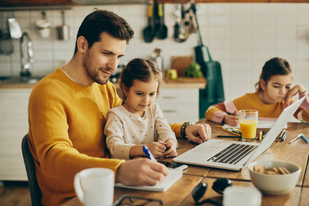 pai trabalhador tomando notas enquanto sua filha pequena está sentada em seu colo em casa. - stay at home dad - fotografias e filmes do acervo