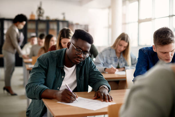 african american university student writing while having test in the classroom. - exam imagens e fotografias de stock