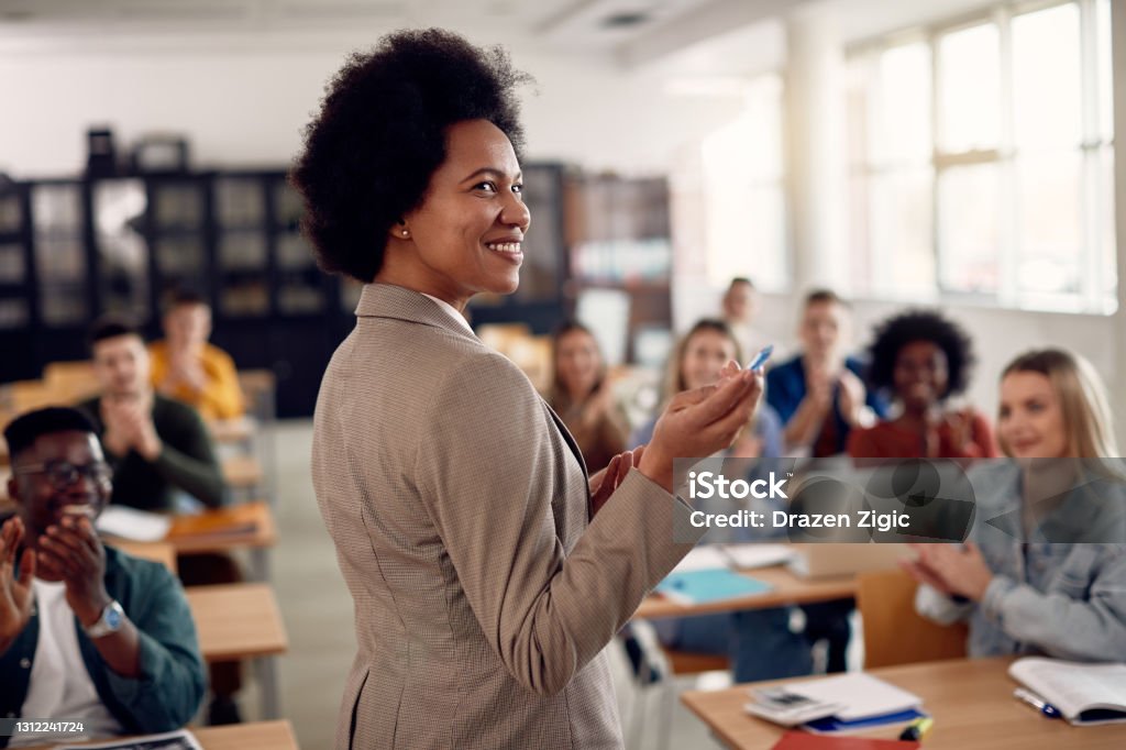 Happy black techer getting applause from her students after giving them a lecture at the university. Happy African American professor receives applause from her students while lecturing them in the classroom. Teacher Stock Photo