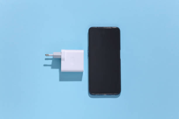 istock Smartphone and charger adapter on  blue bright background with deep shadow. Top view. Flat lay. Minimalism 1312241808