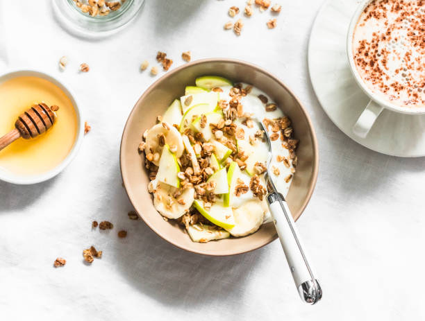 iogurte grego com granola, banana, maçã, mel em um fundo leve, vista para cima. café da manhã delicioso - granola oatmeal cereal fruit - fotografias e filmes do acervo