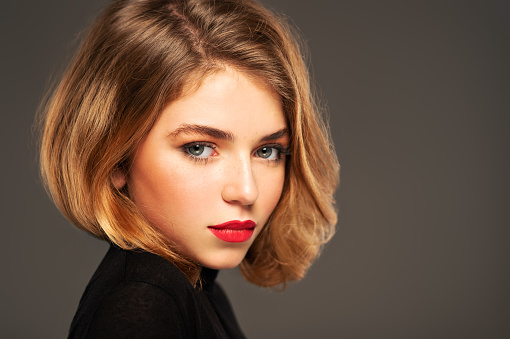 Closeup portrait of an young adult girl with medium length hair.  Photo of a fashion model posing at studio. Pretty young woman with red lips looking at camera. Beauty portrait.