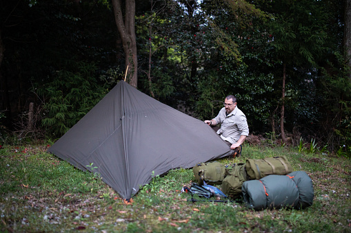 A man is erecting a tarp shelter in the woods.