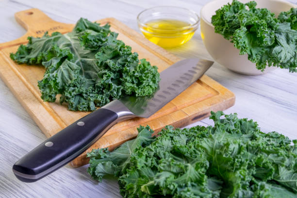 Kale leaves in a large kitchen knife on a wooden cutting board