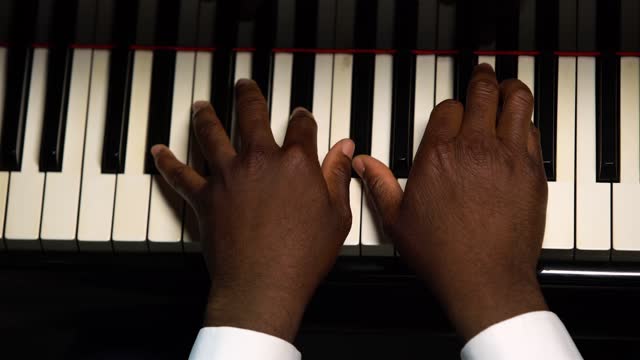 Top view of male hands playing the grand piano. The African American touches the black and white keys with his fingers to create the rhythm of the melody. Close up black hands of a male pianist