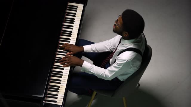 Top view of stylish man playing grand piano. The African American touches the black and white keys with his fingers to create the rhythm of the melody. Close up of a black male pianist