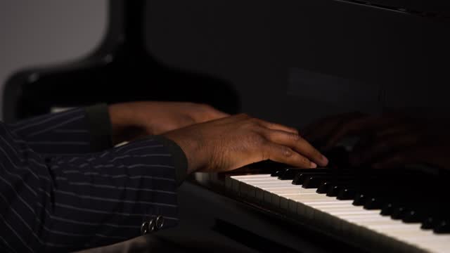 Side view of male hands playing the grand piano. The African American touches the black and white keys with his fingers to create the rhythm of the melody. Close up black hands of a male pianist