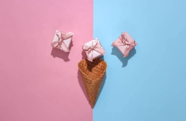 istock Ice cream waffle cone with gift boxes on pink and blue bright pastel background with deep shadow, top view. Flat lay minimal composition 1312251541