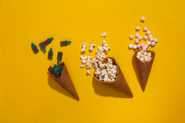 istock Ice cream waffle cones with marshmallows, gummy candy and popcorn on yellow background with deep shadow, Top view, Flat lay, Pop art 1312251562