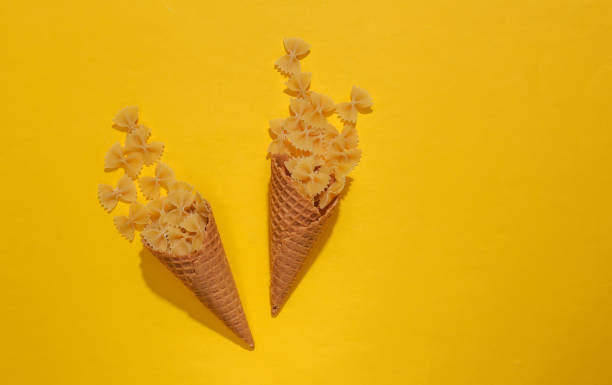 istock Ice cream waffle cones with pasta bows on yellow bright background with deep shadow, top view. Flat lay minimal composition 1312251595