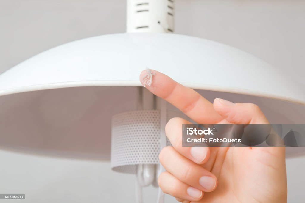 Young adult woman finger showing dust from top of white lamp shade in room. Closeup. Front view. Checking cleanliness quality. Dust Stock Photo