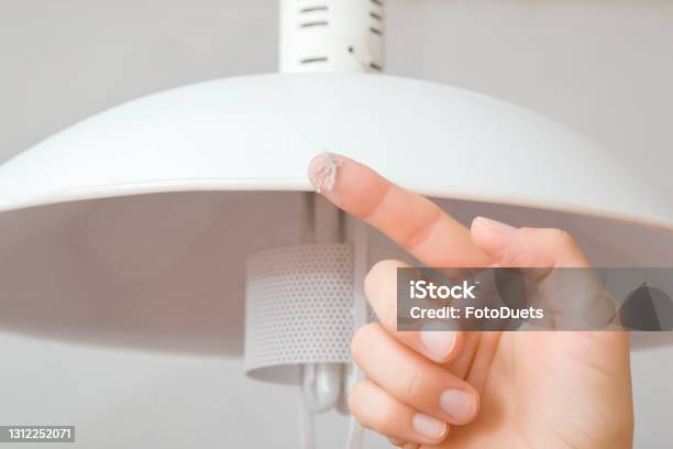 Young Adult Woman Finger Showing Dust From Top Of White Lamp Shade In Room Closeup Front View Checking Cleanliness Quality Stock Photo - Download Image Now