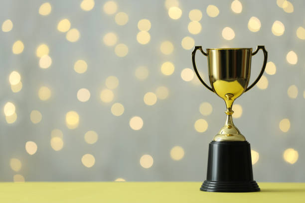 istock Golden trophy cup on table against blurred lights. Space for text 1312256608