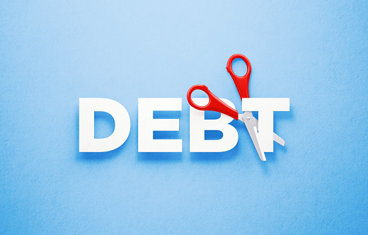Red scissors cutting the word debt over blue background. Horizontal composition with copy space. Cutting debts concept.