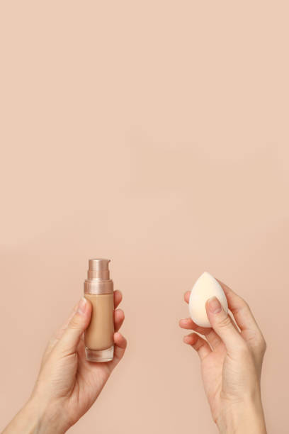 istock Applying foundation on makeup sponge. Woman's hands with neutral manicure holding bottle of concealer or toner foundation, cream and beauty blender, make up artist background 1312261084