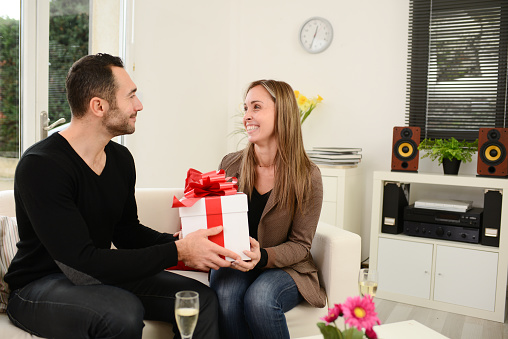 Young attractive couple dating during valentine's day and offering each other gifts at home in living-room